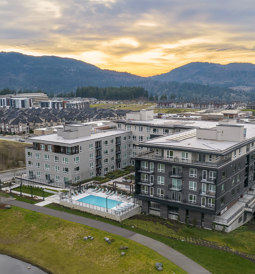 Aerial view of apartment buildings with a pool at sunset, backed by mountains and a cloudy sky