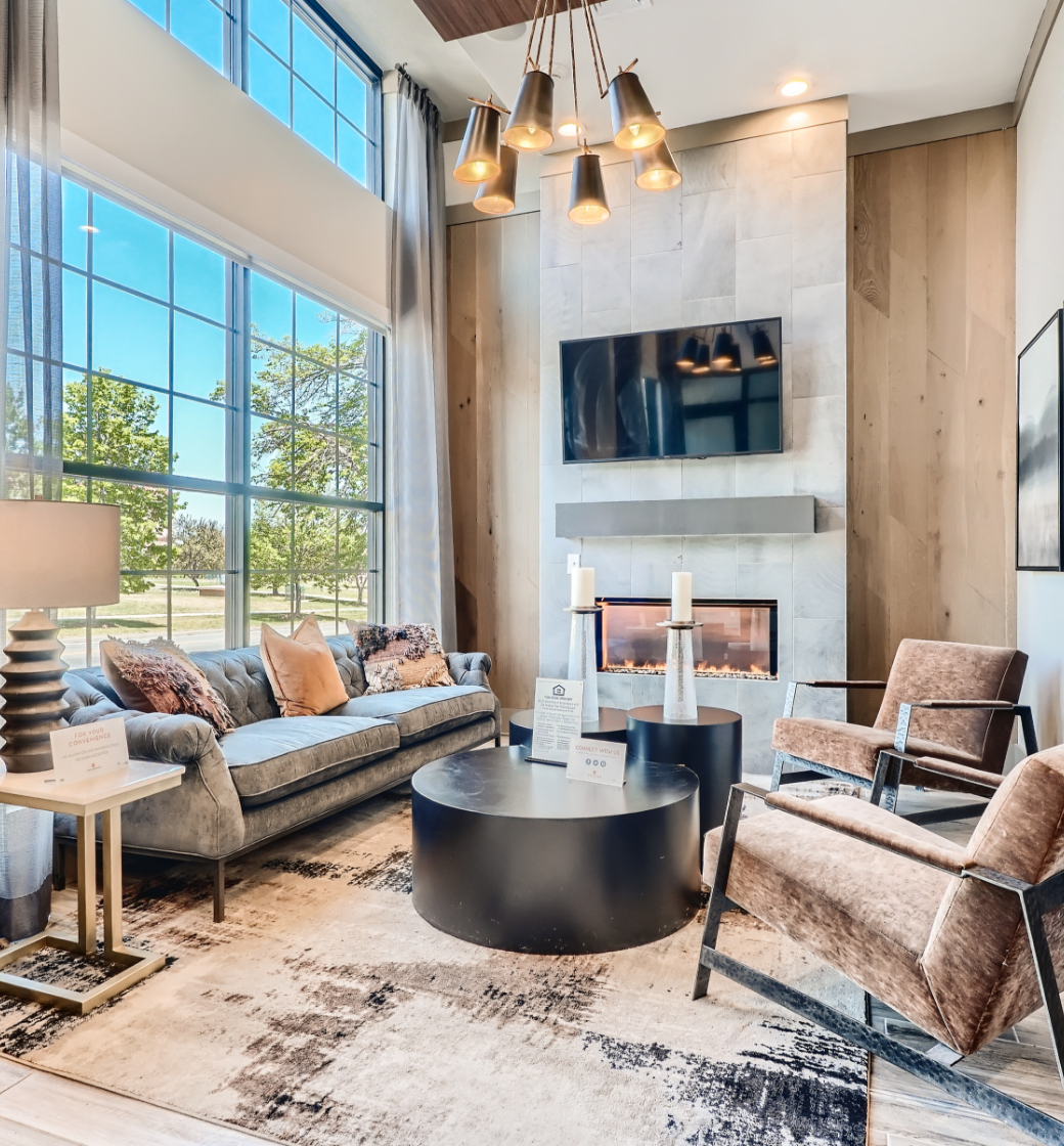 Bright modern living room with tall windows, fireplace, TV, and neutral furniture on a patterned rug