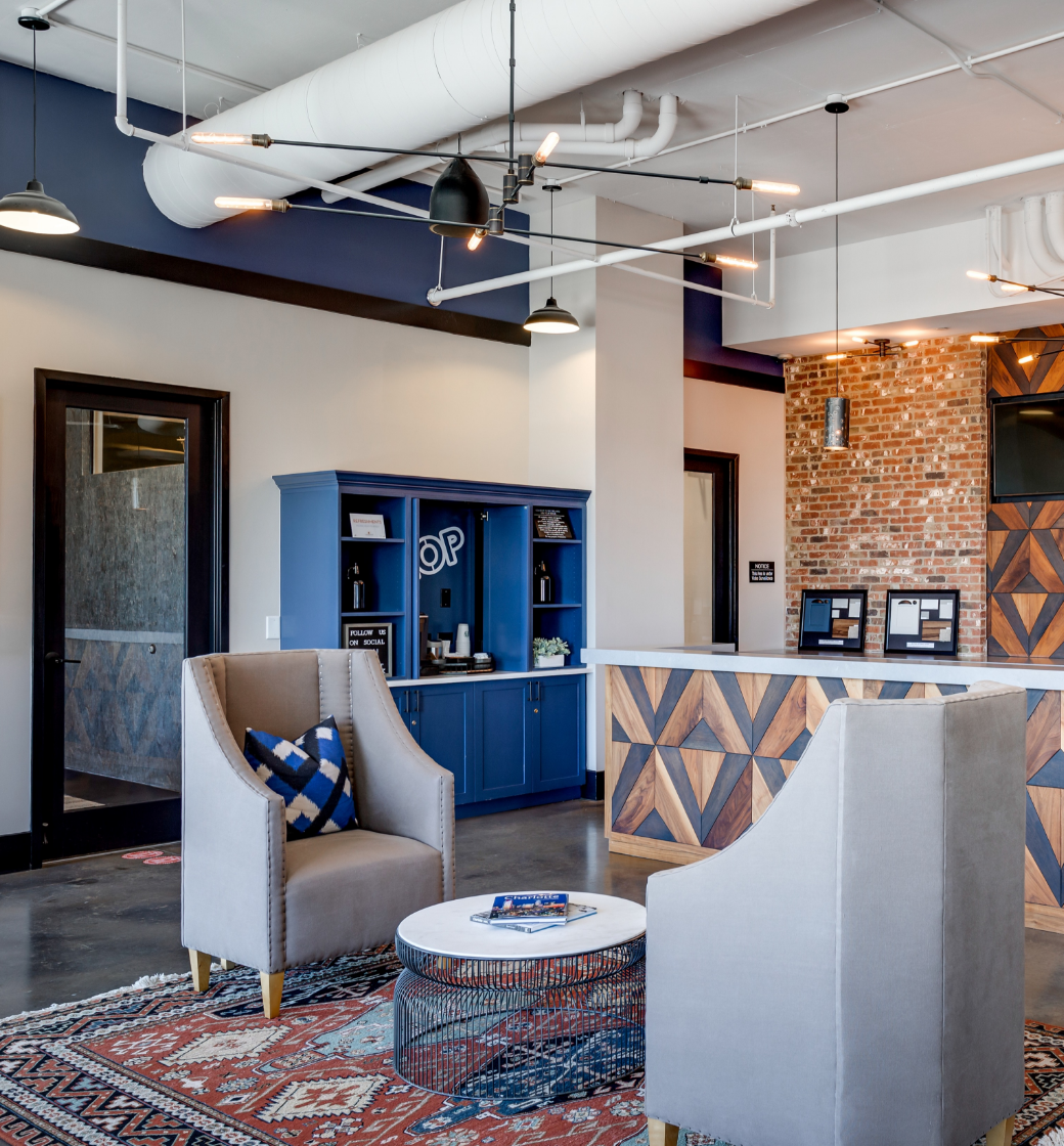 Modern office lounge with blue cabinetry, gray chair, patterned rug, and exposed brick accents