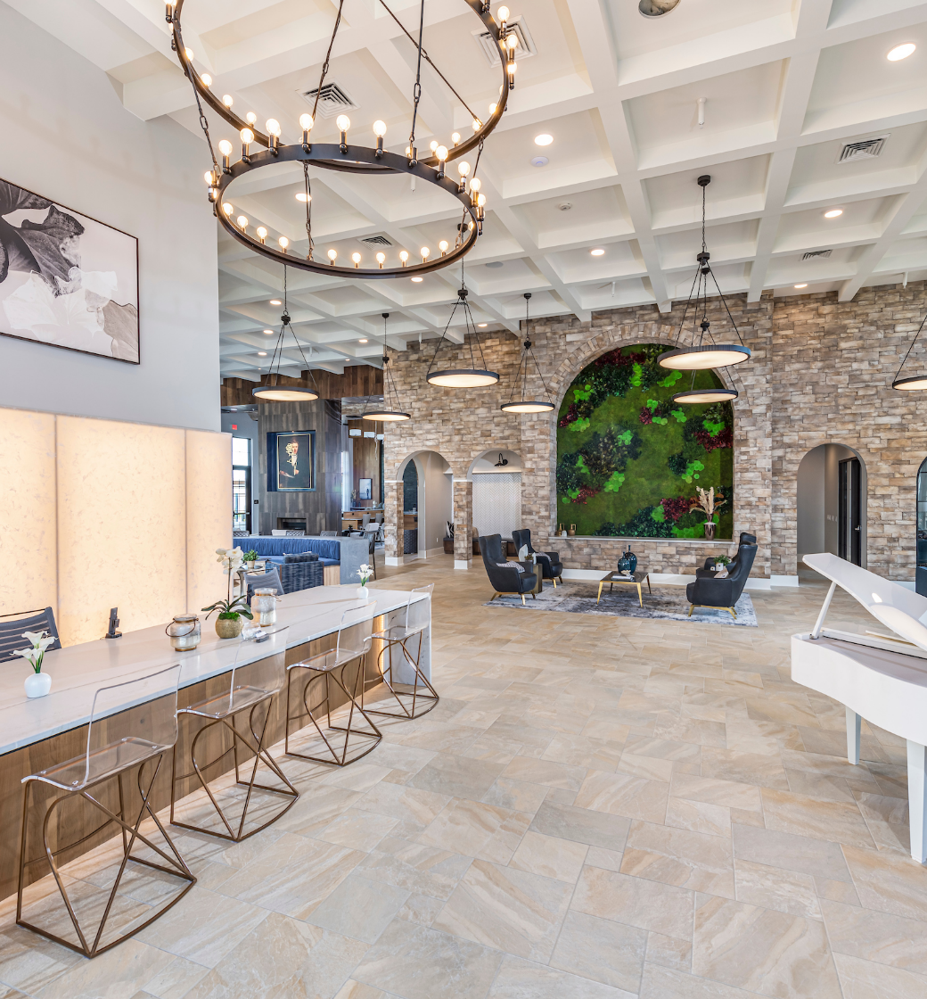Bright modern lounge with stone walls, large circular chandelier, and white tables in a spacious tiled room