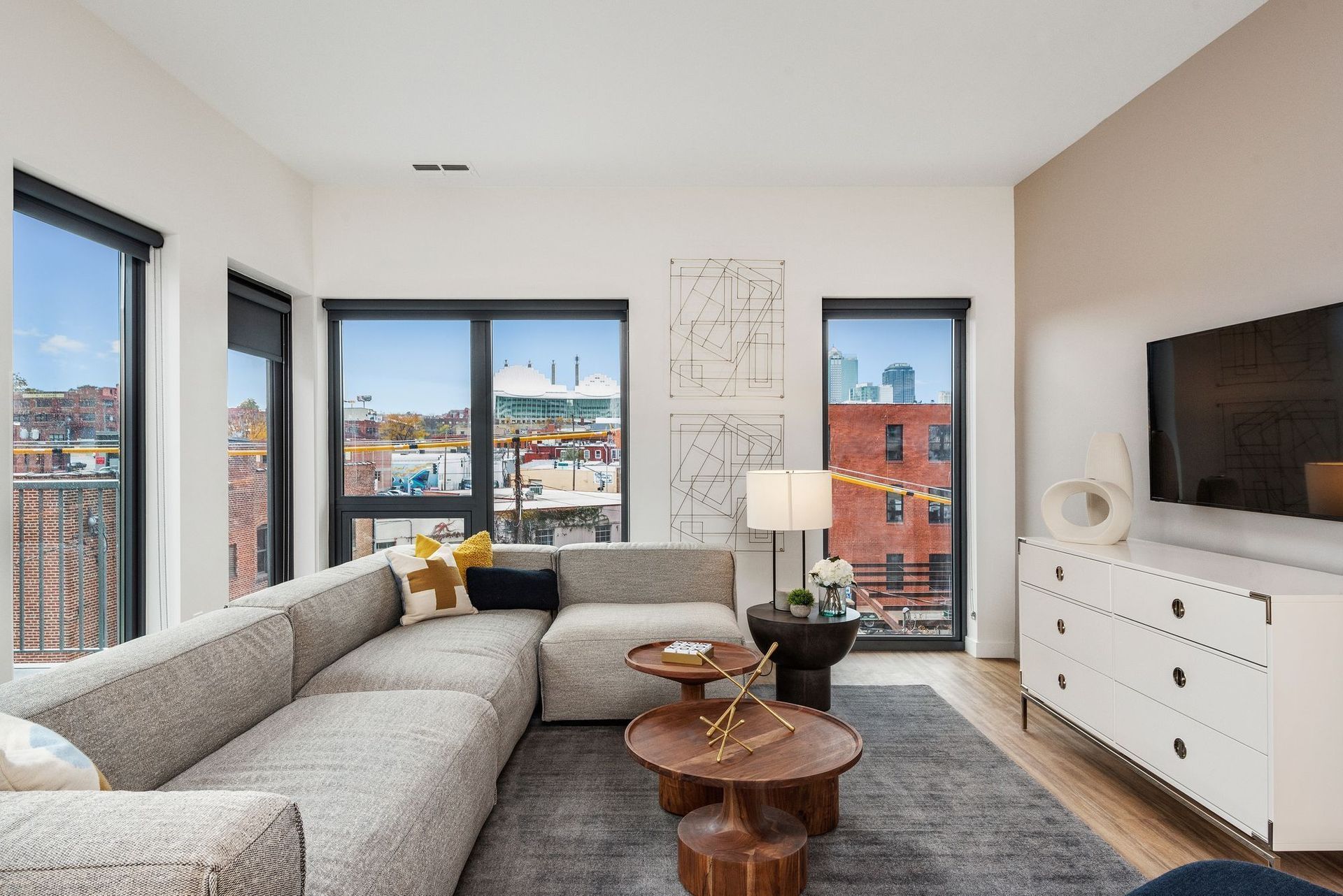 Modern living room with sectional sofa, coffee tables, and cityscape view.