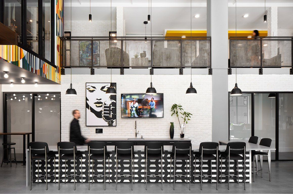 Modern bar area with long counter, stools, TV, and person walking by.