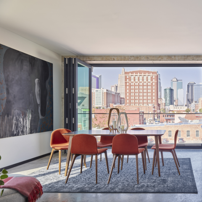 Dining area with red chairs, table, and cityscape view. Large abstract artwork on wall.