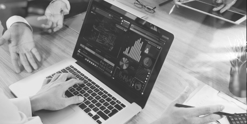 Black and white image of two people discussing on the table with a laptop showing charts.