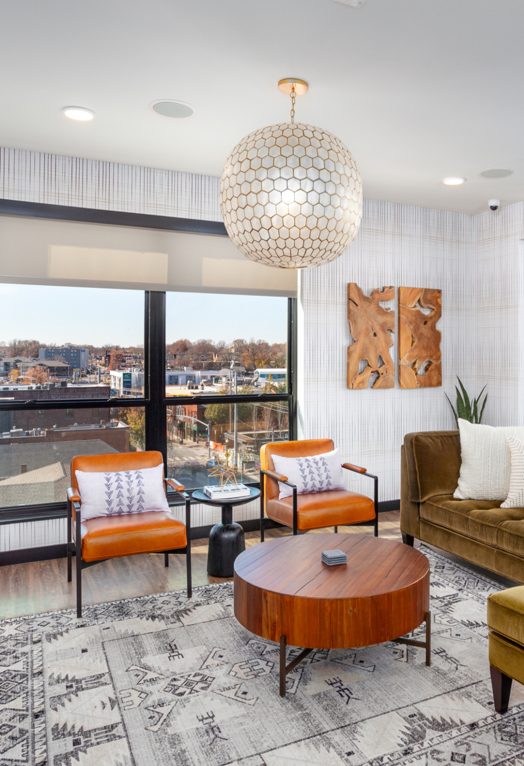 Modern living room with orange chairs, round wooden coffee table, and large windows overlooking water