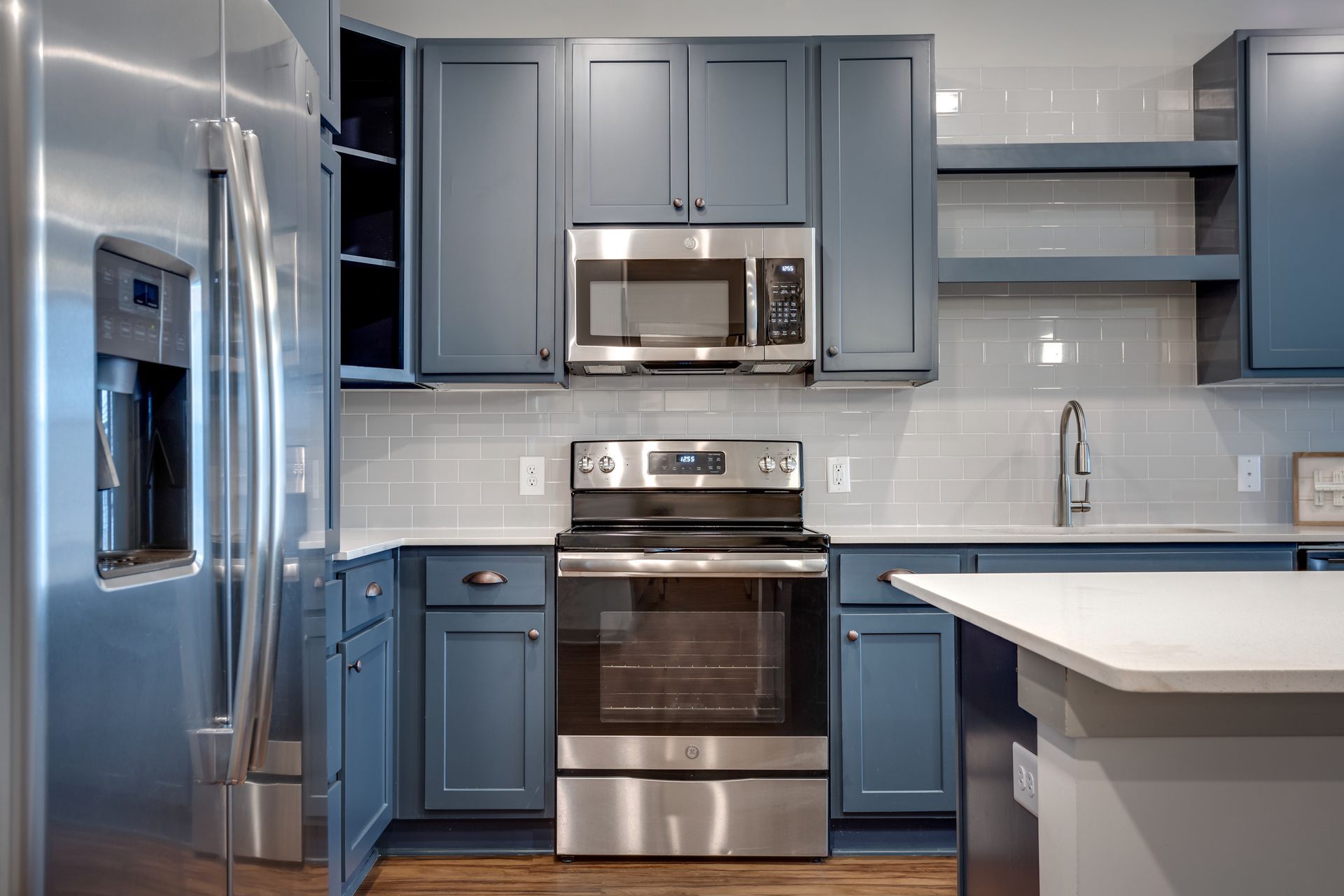 Blue kitchen with stainless steel appliances, white countertop, and light gray backsplash.
