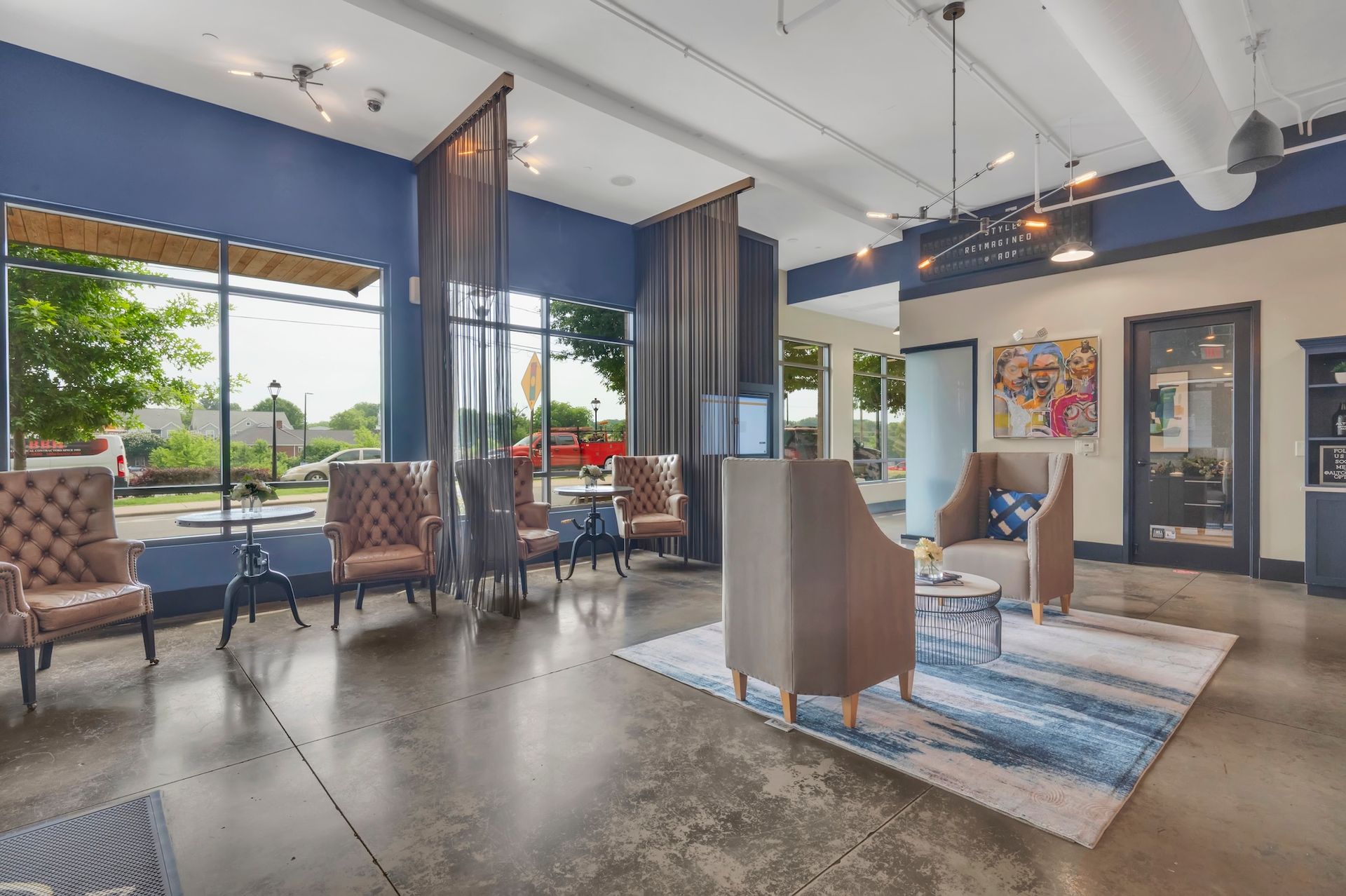 Modern waiting area with chairs, large windows, colorful wall art, and a rug over polished concrete floor