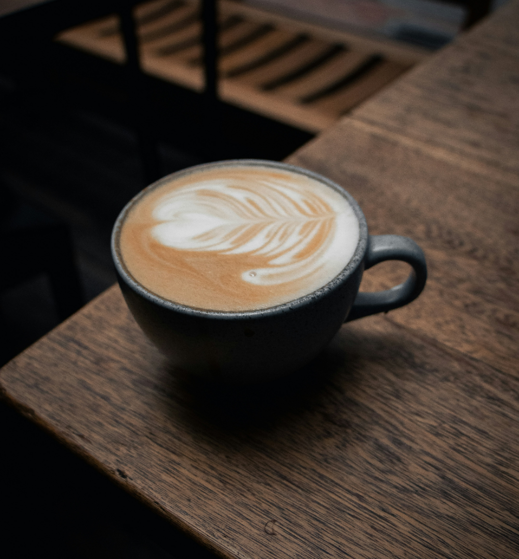 Latte with leaf latte art in a dark cup on a wooden table