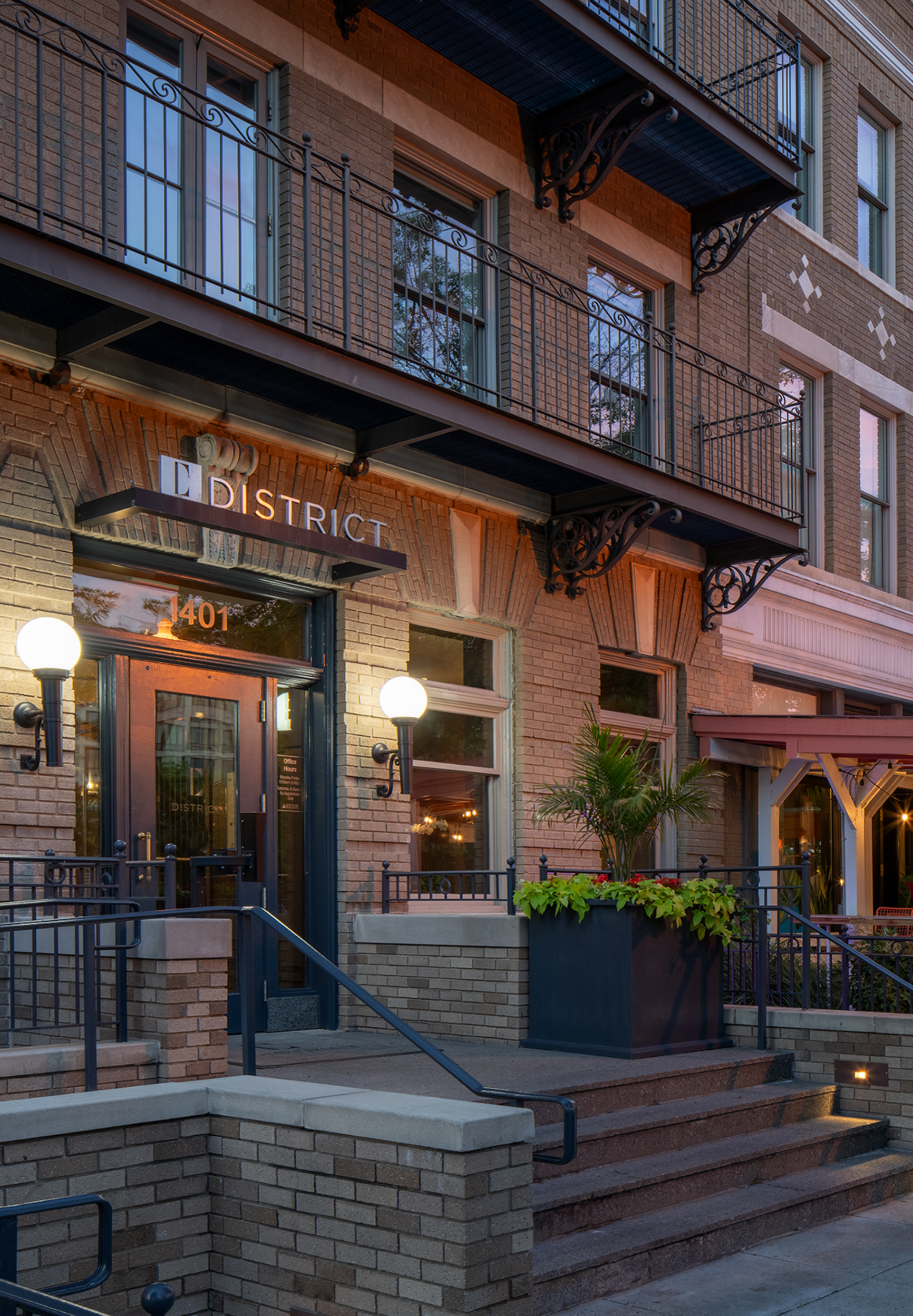 Brick apartment building entrance with stairs, balconies, and lit lamps at dusk