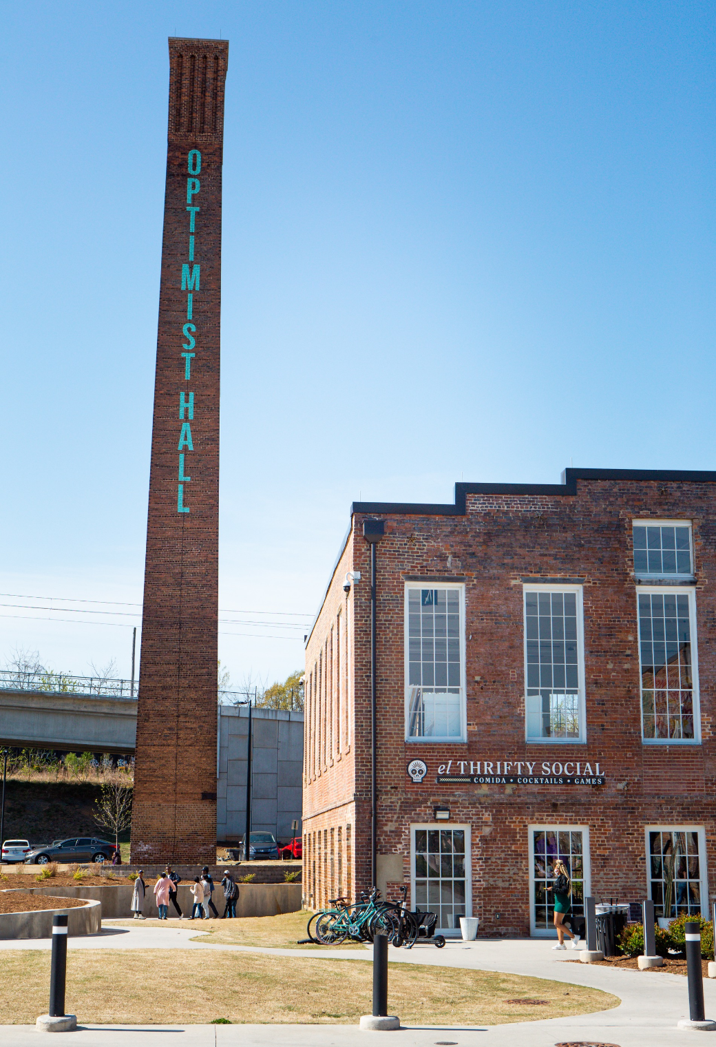 Brick industrial building with tall chimney tower and turquoise vertical lettering under a clear blue sky