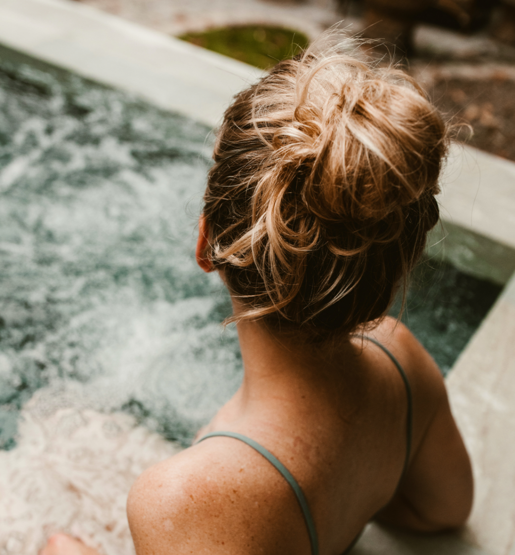 Person relaxing in a bubbling hot tub, seen from behind with hair in a bun.