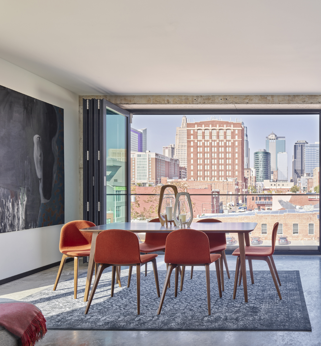 Modern dining room with orange chairs, round table, and city skyline view through large windows