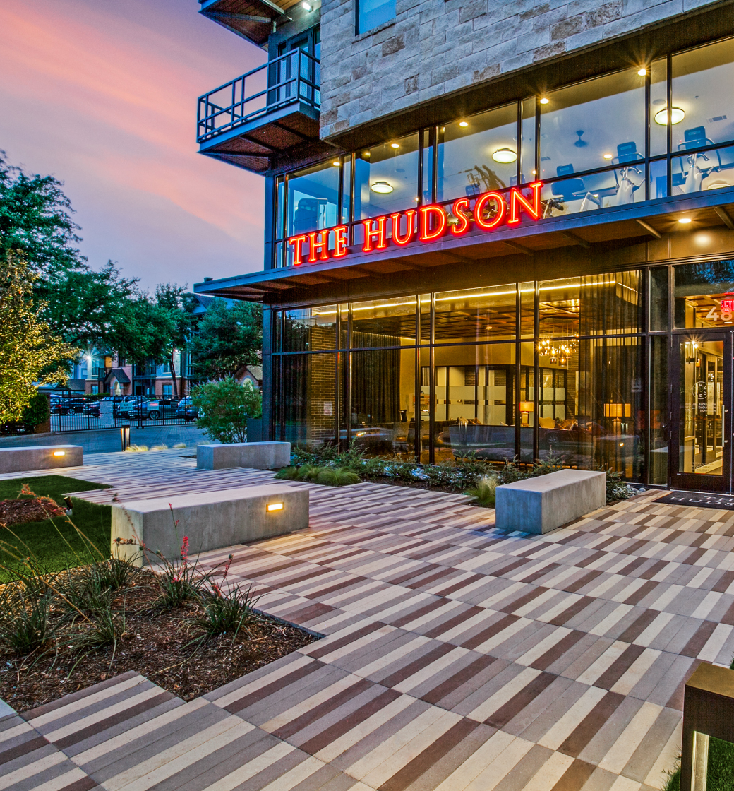 Exterior of The Hudson restaurant at dusk with glass frontage, red sign, and striped walkway