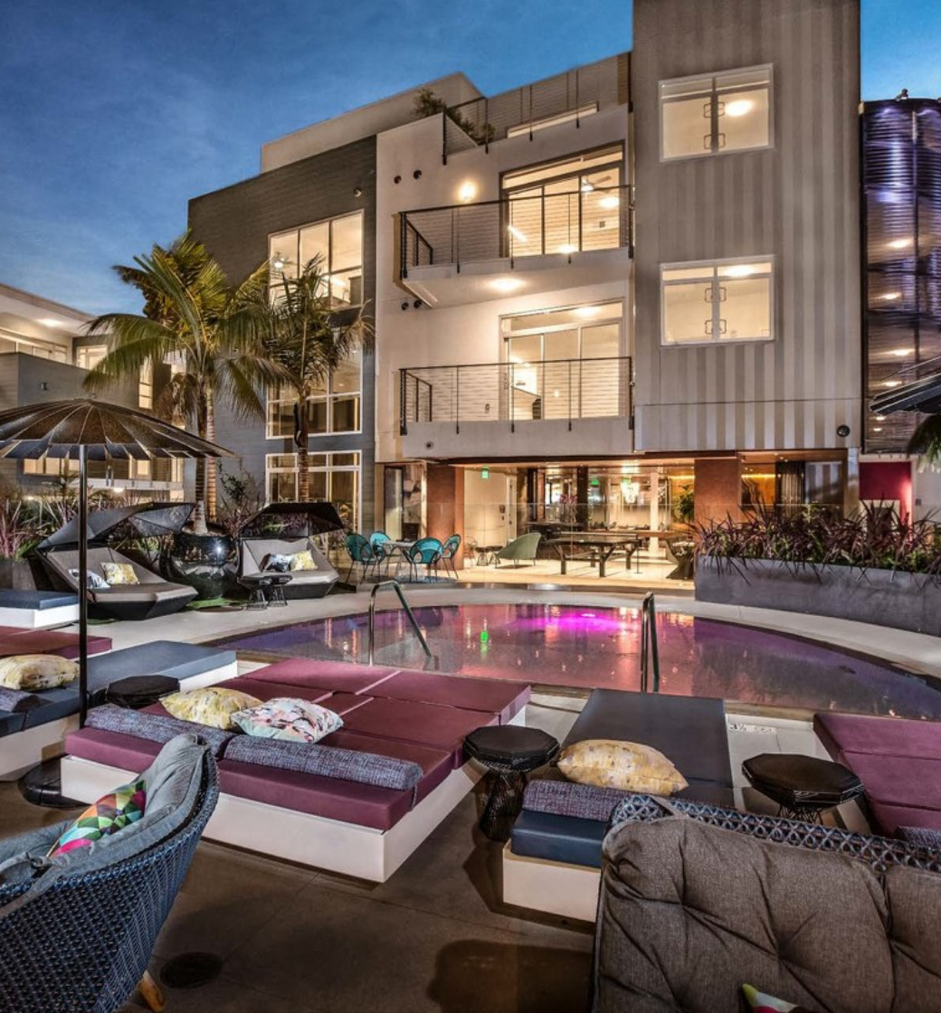 Modern apartment courtyard with lounge seating, pool, and lit balconies at dusk