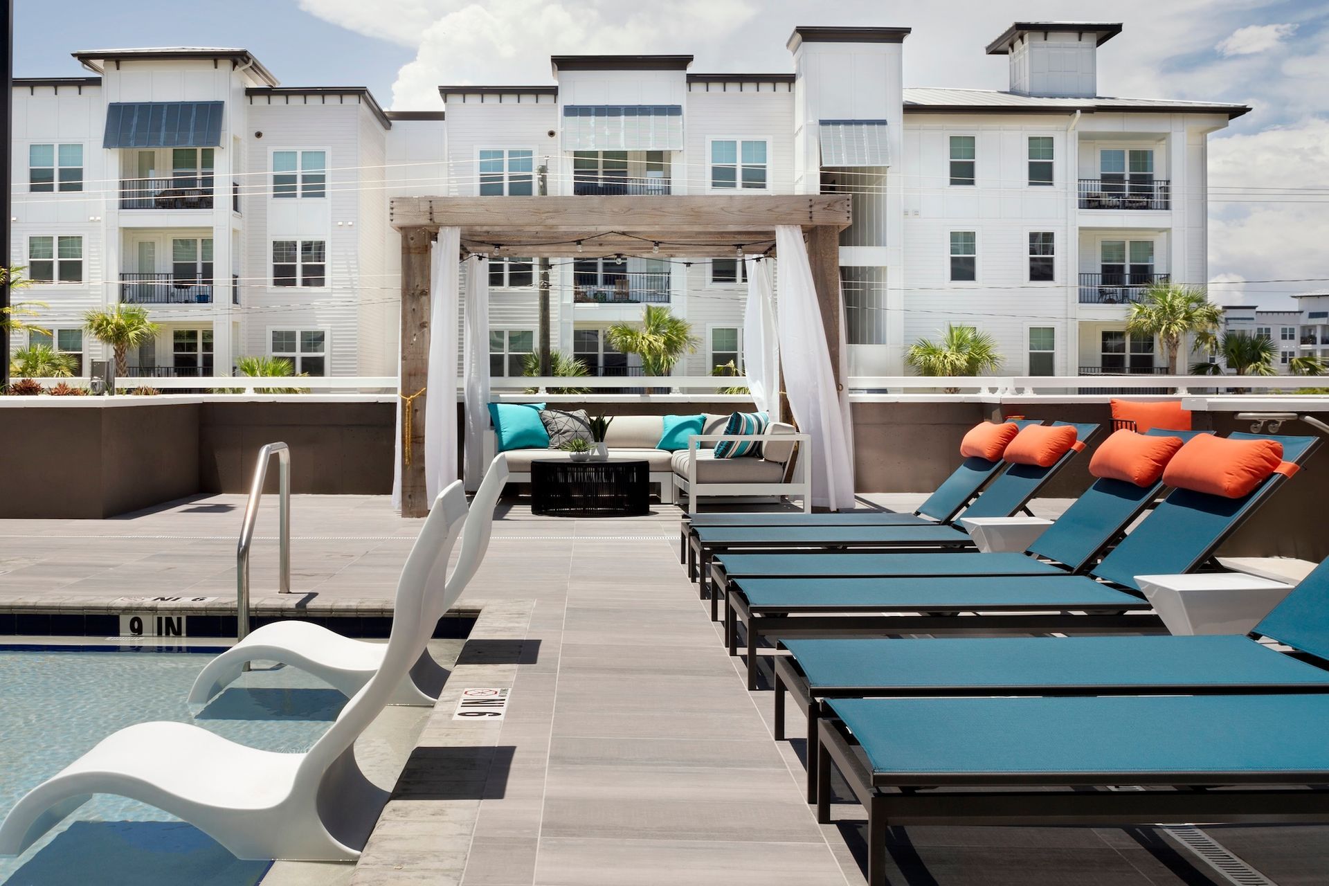 Rooftop pool deck with lounge chairs and cabanas in front of a modern apartment building