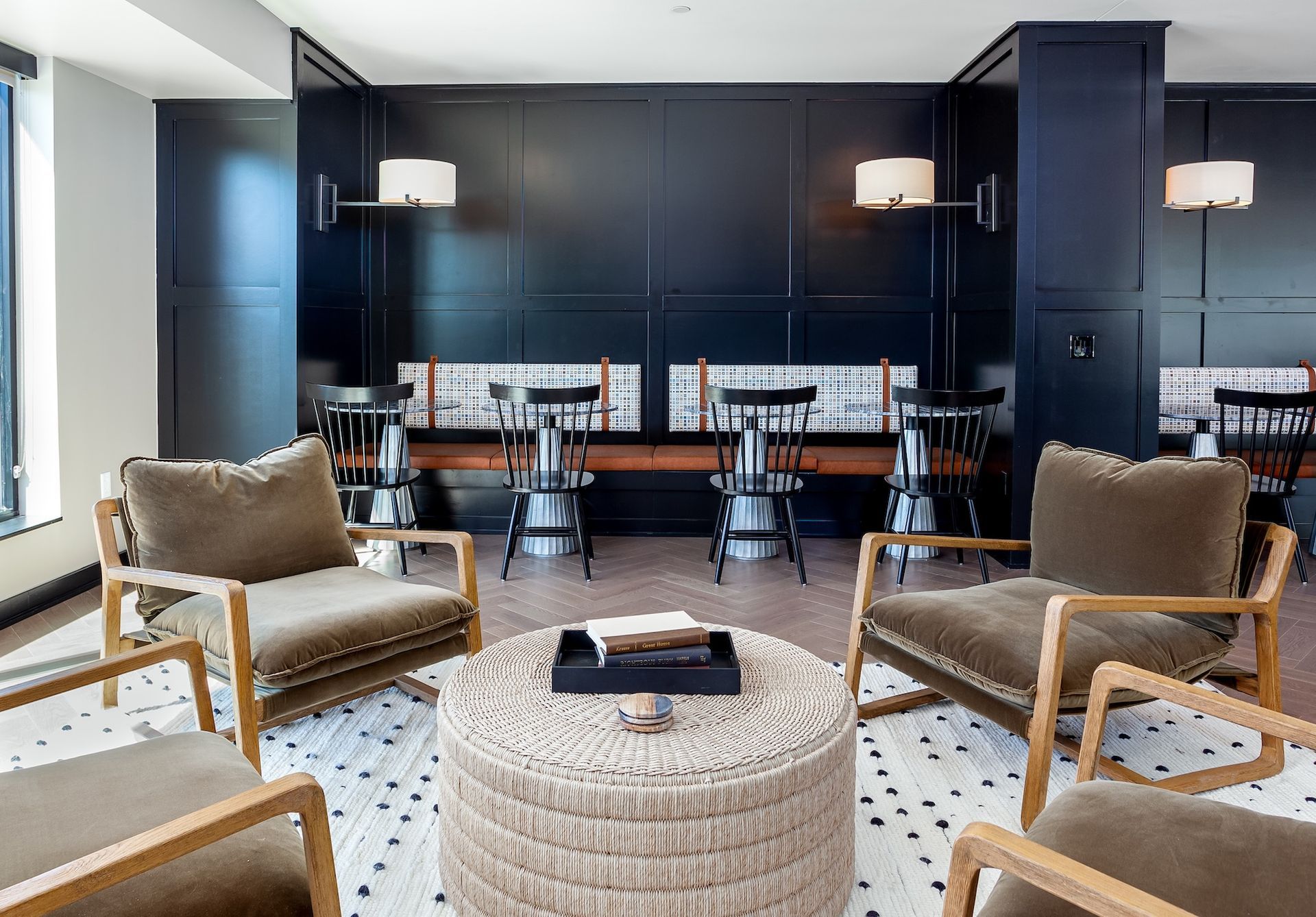 Modern lounge with dark wall paneling, tan chairs, and a woven coffee table in a bright room