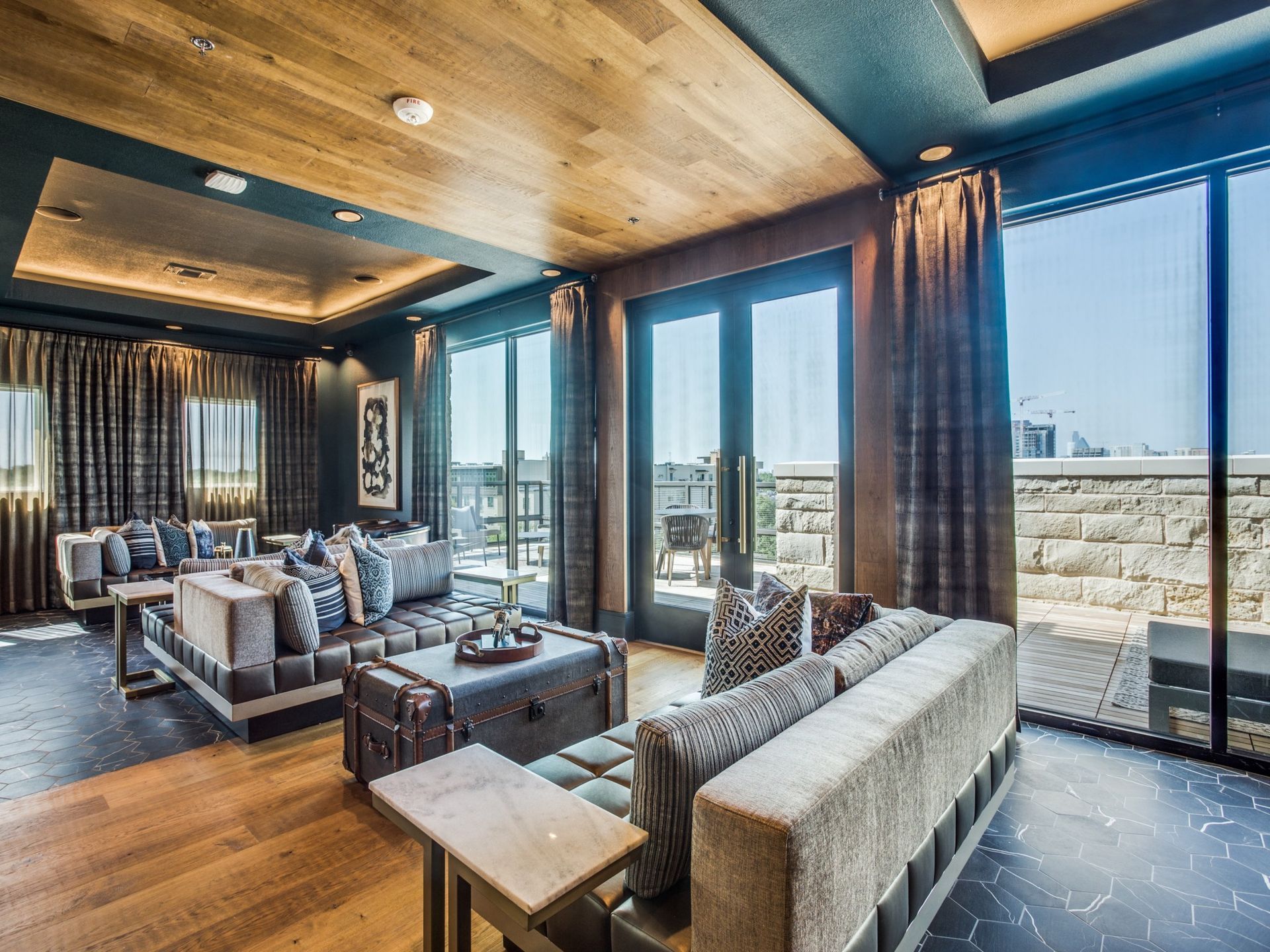 Luxurious living room with wooden ceiling, blue walls, large windows, and modern gray furniture.