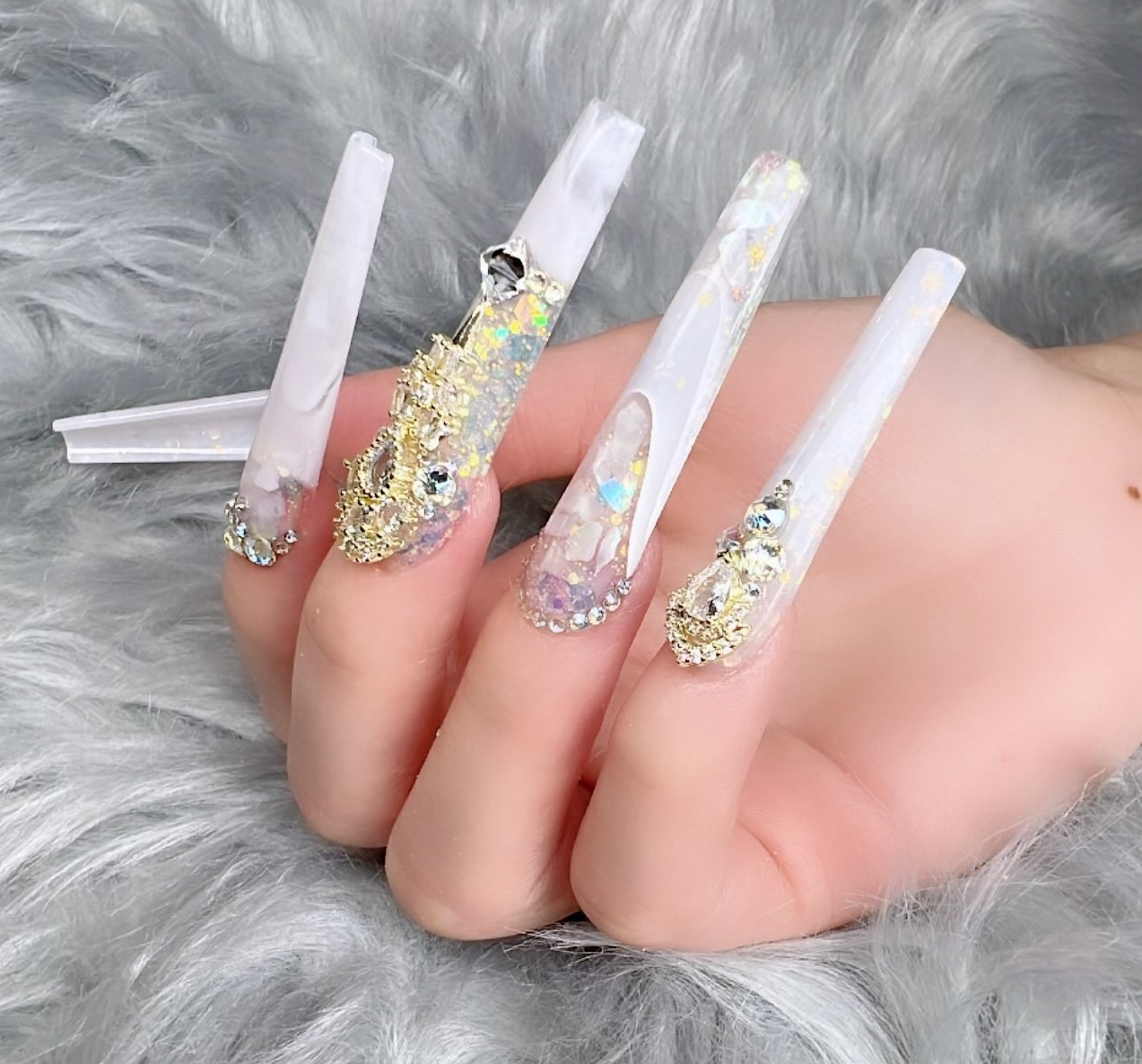 A woman 's hand with long white nails and rhinestones on them.