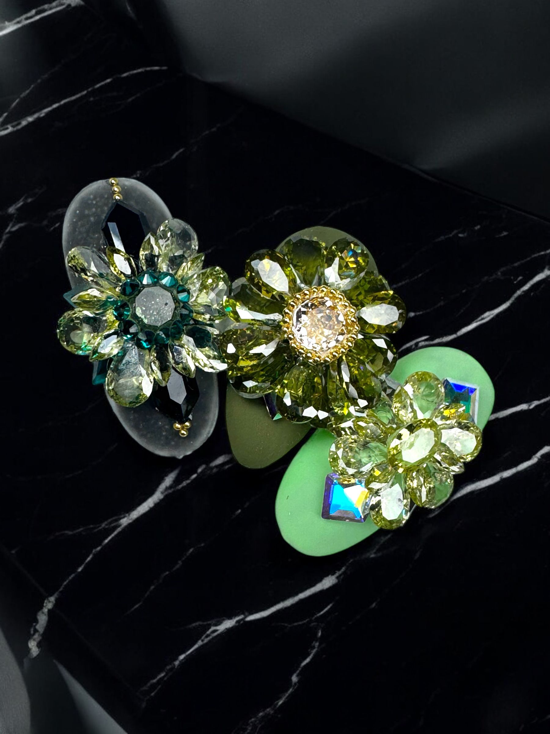 A pair of green earrings are sitting on a black marble surface.