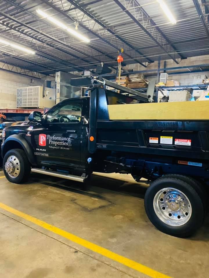 Blue dump truck parked inside a warehouse garage with fluorescent lights and yellow floor lines