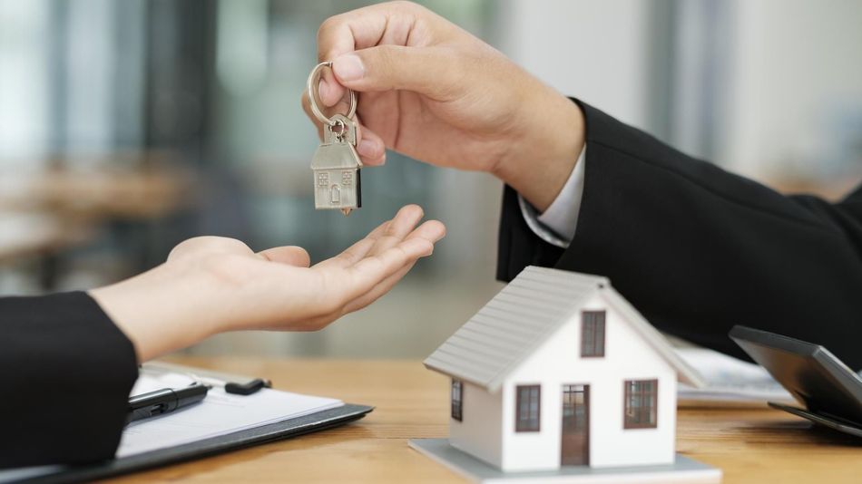 Handing over house keys during a home sale, with a small model house on the table
