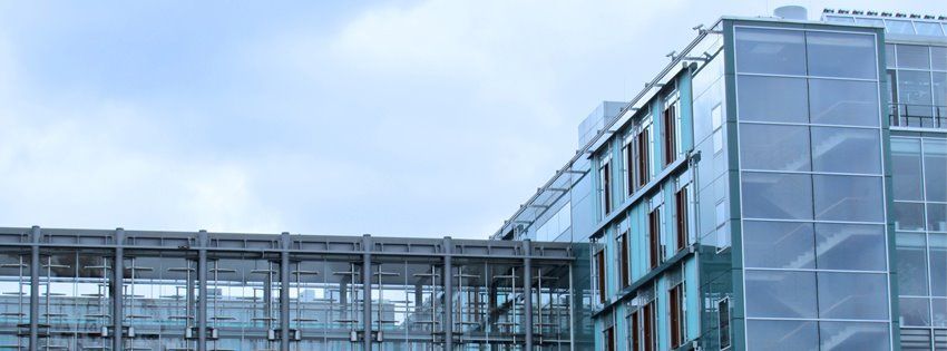 Modern glass office building with skybridge under a cloudy sky