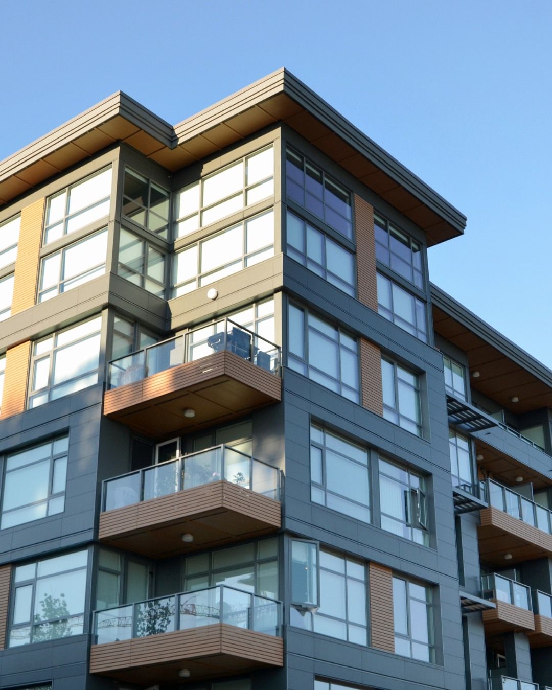 Modern apartment building with glass balconies and gray siding under a clear blue sky