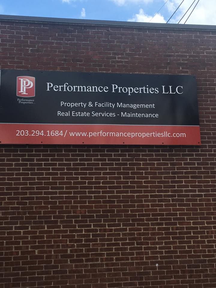 Performance Properties LLC sign on a brick wall, with website and phone number on a red panel.