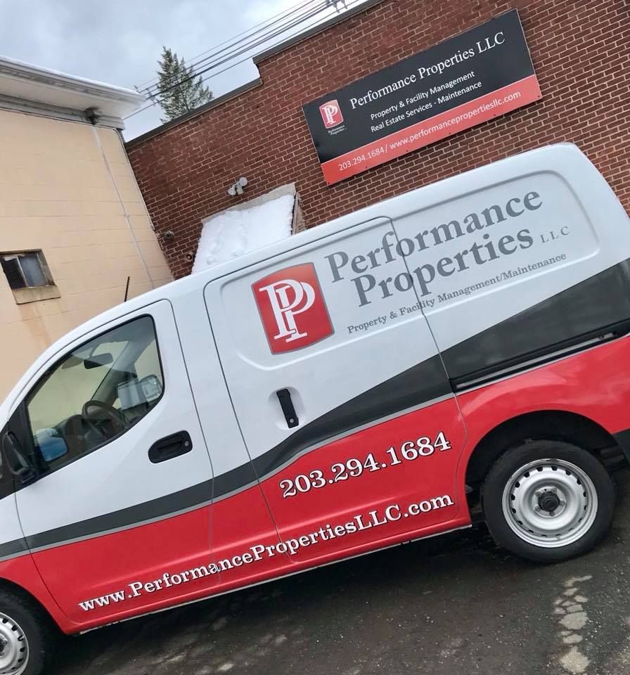 White-and-red Performance Properties LLC van parked by a brick building with matching company sign.