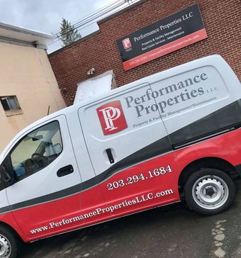 White and red Performance Properties LLC work van parked by a brick building with company sign.