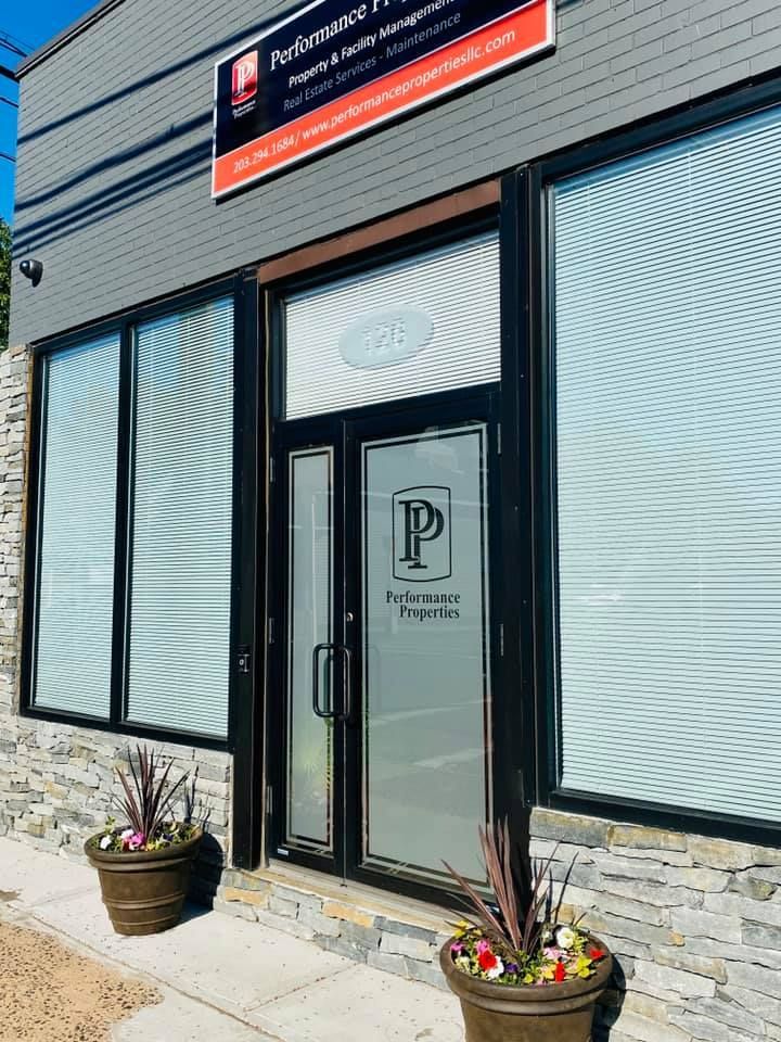 Storefront entrance with glass door, frosted windows, and potted flowers beside the steps