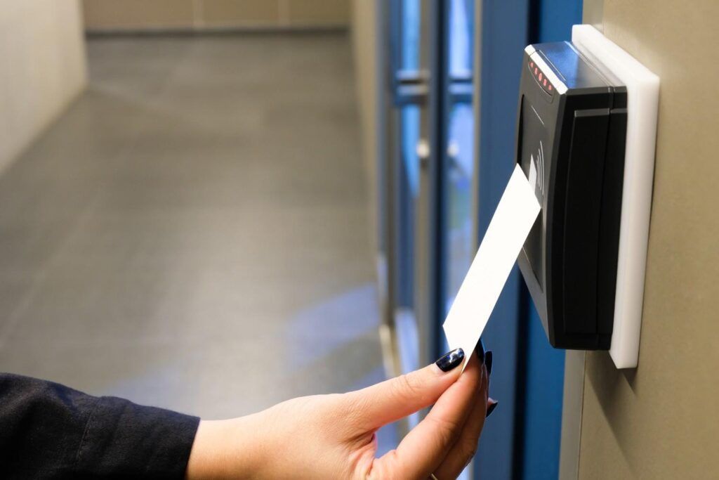 Hand inserting a white keycard into a wall-mounted card reader in a hallway