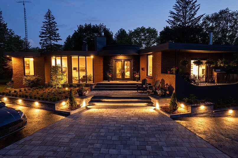 Modern single-story house at dusk with warm exterior lights and a stone driveway