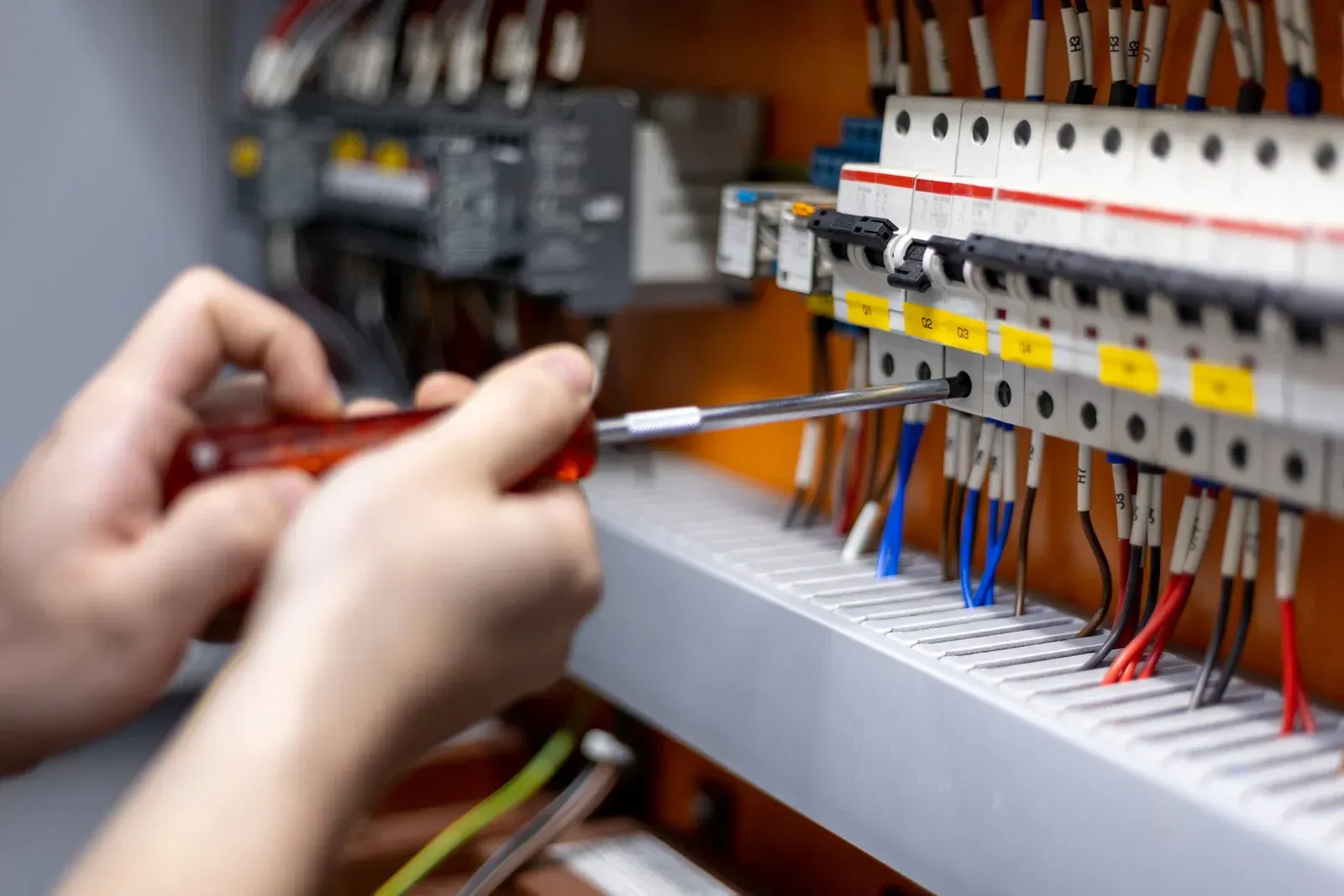 Hands adjusting wires in an electrical control panel with a screwdriver