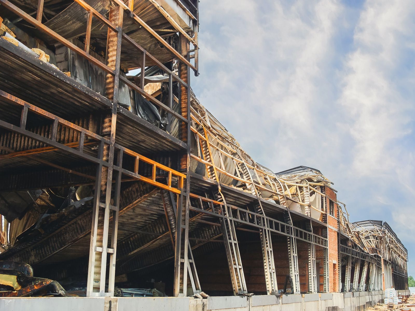 Damaged industrial structure with collapsed steel beams and debris against a cloudy sky