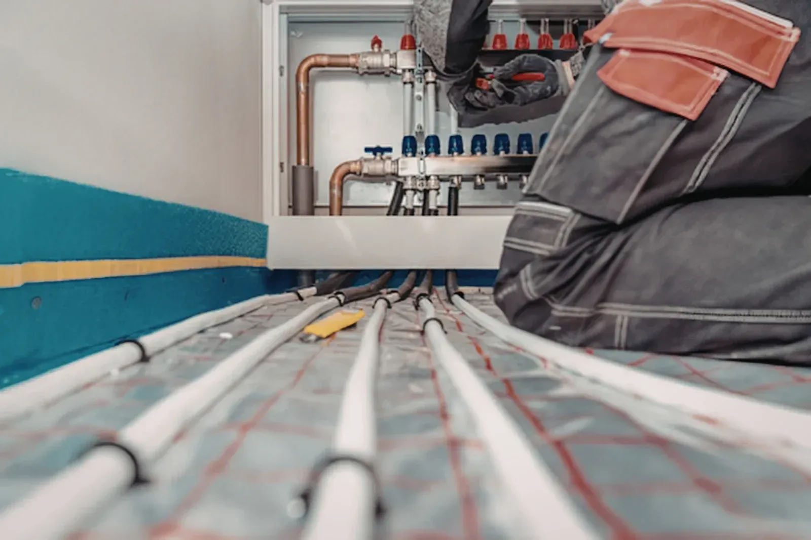 Worker inspecting cables in a utility room with pipes and electrical panels