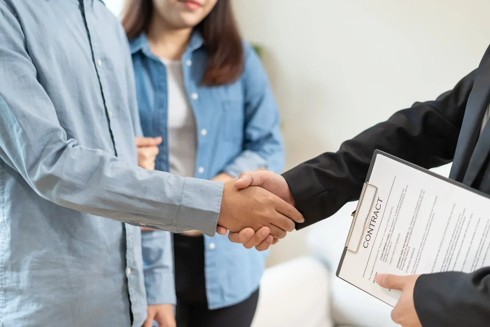 Two people shaking hands in an office, with another person holding documents nearby