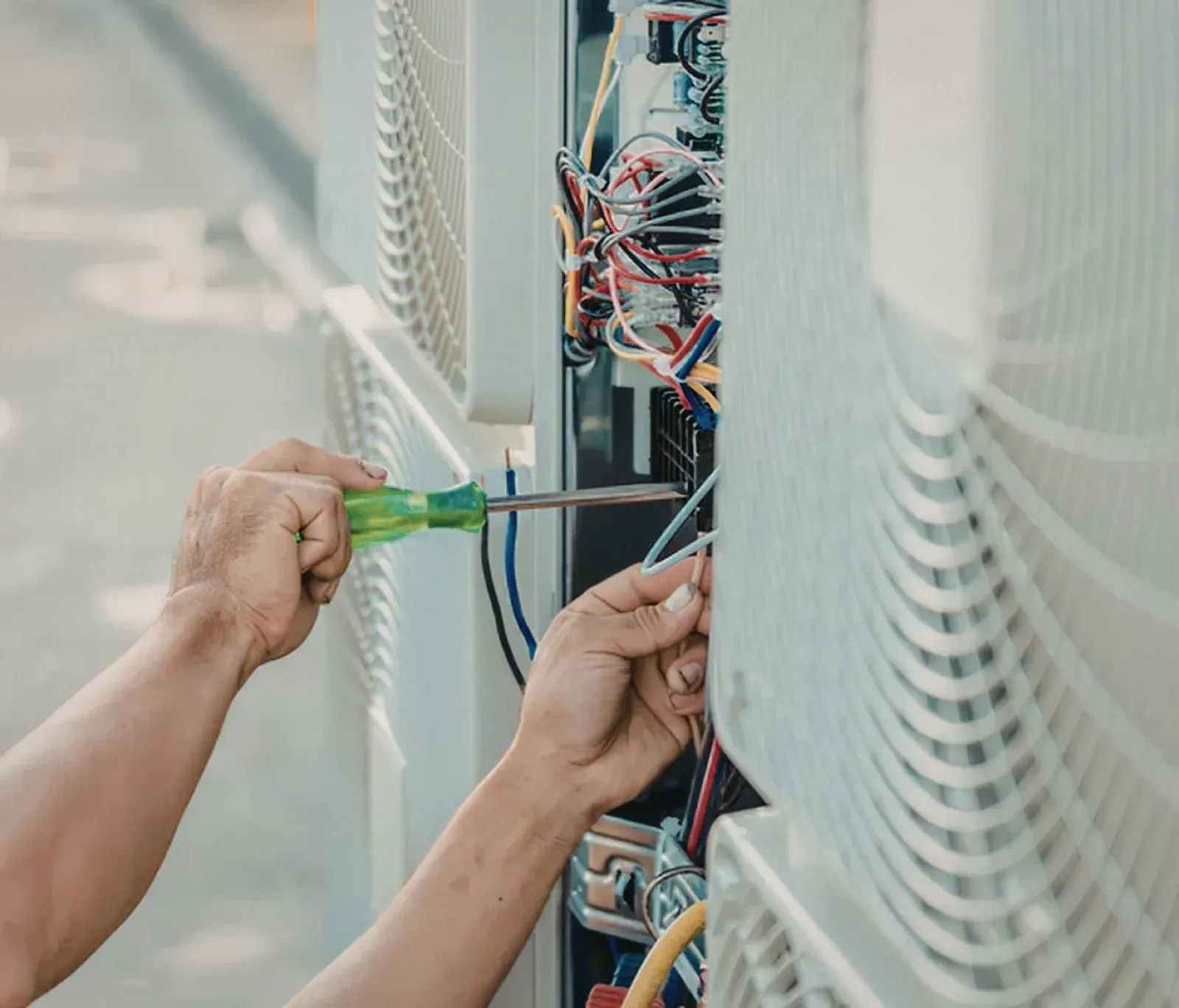 Hands using screwdrivers to work on exposed electrical wiring in a wall-mounted cabinet