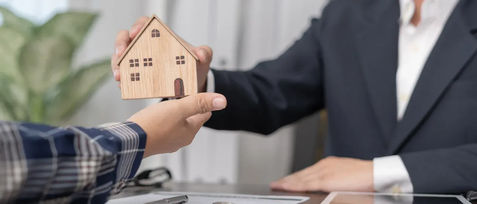 Handing over a small wooden house model during a real estate meeting