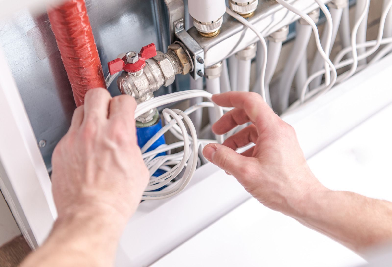 Hands adjusting network cables and plumbing pipes inside a utility panel