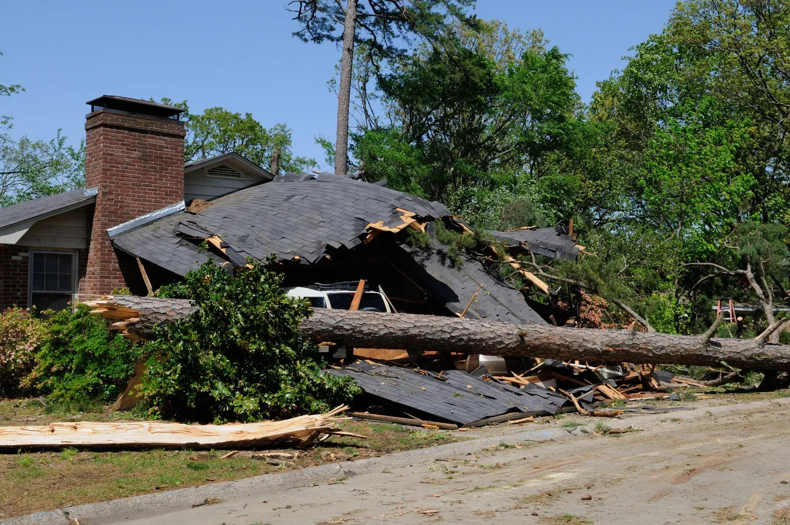 Collapsed house roof with debris and fallen tree blocking a street after storm damage