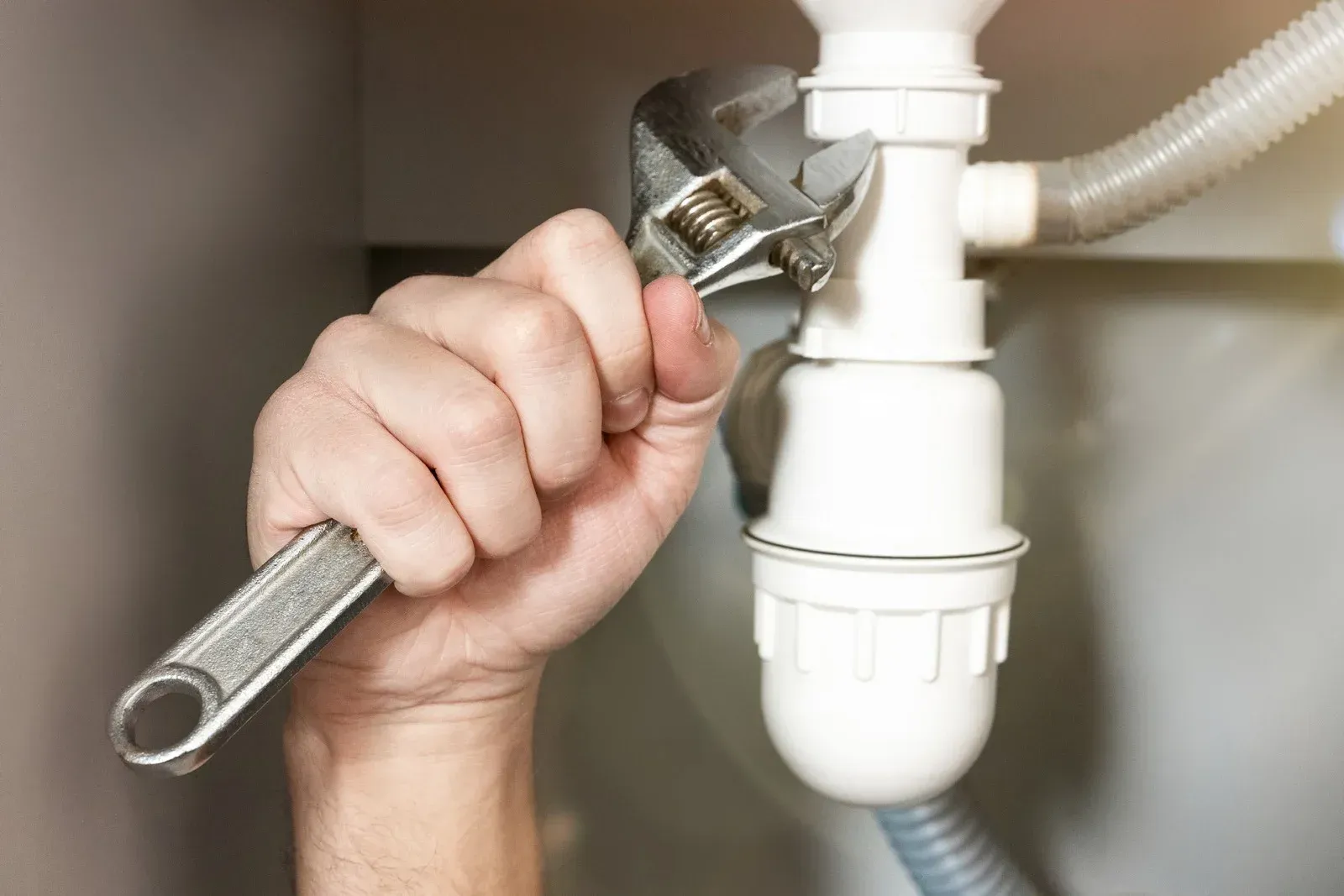 Hand tightening a pipe fitting under a sink with a wrench