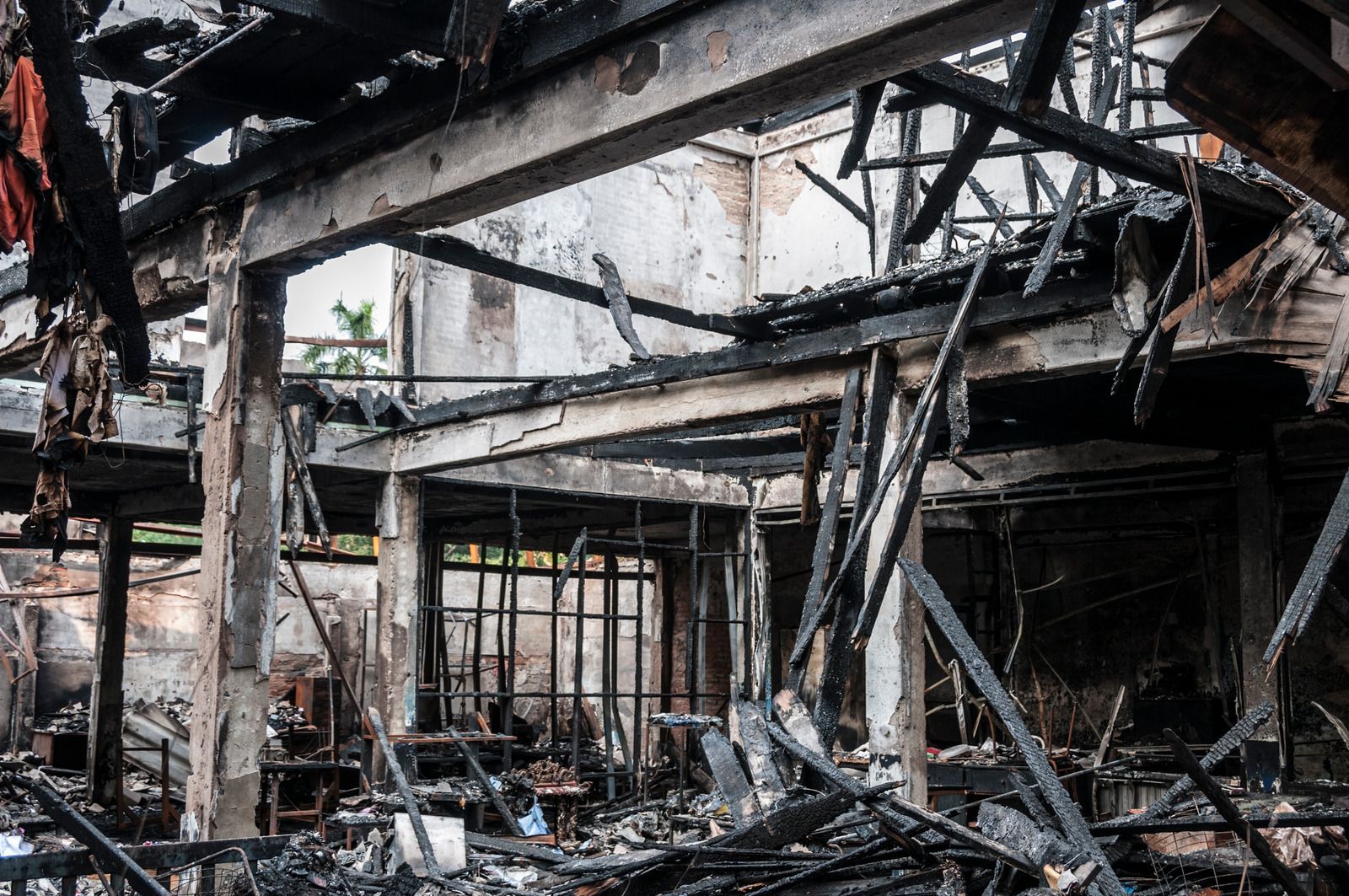 Burned-out industrial building interior with charred beams and debris scattered across the floor