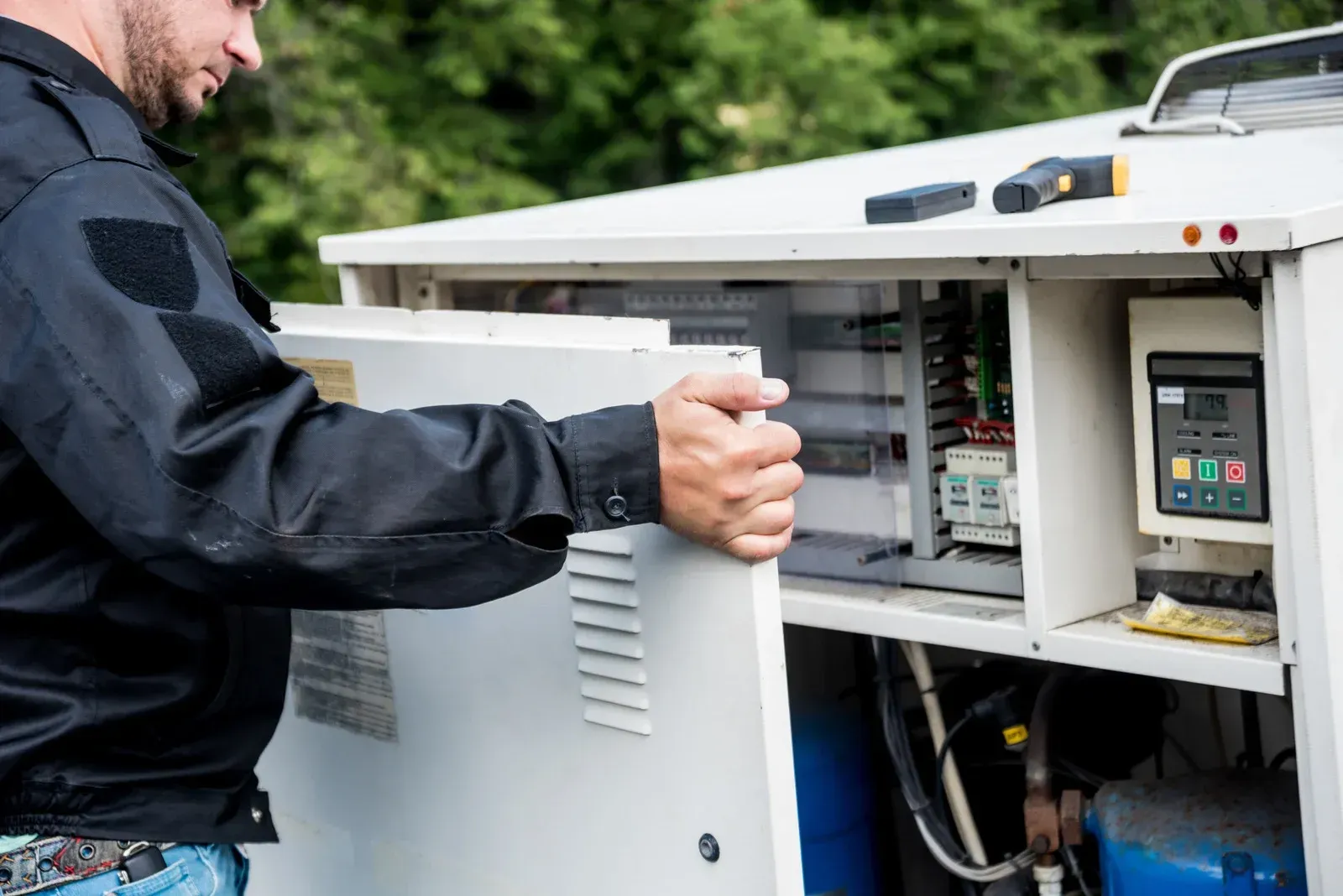 Technician opening an industrial cabinet with electrical equipment inside and wiring visible