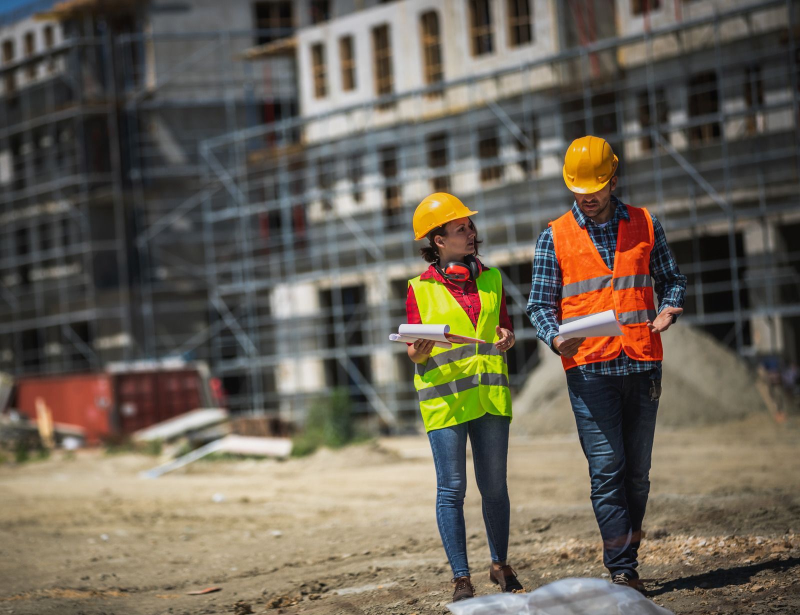 Two construction workers in hard hats and safety vests walking at a building site