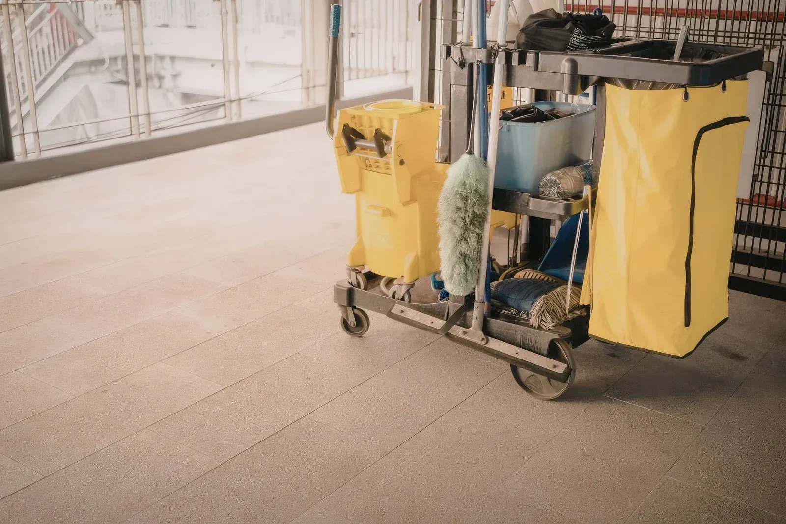 Yellow janitorial cart with cleaning supplies on a carpeted floor near a bright windowed wall