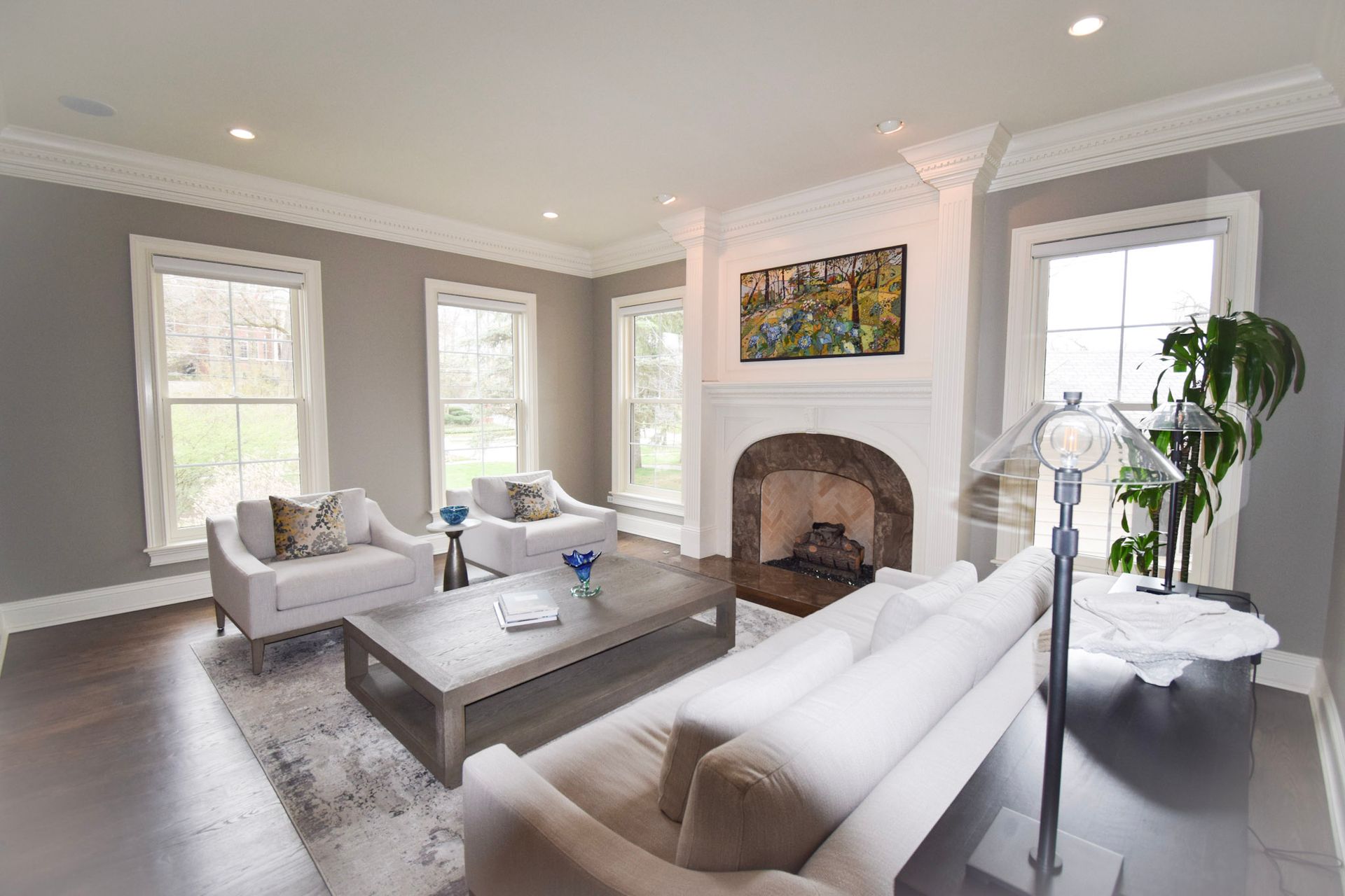 Living room with white furniture, fireplace, and large windows. Gray walls, dark wood floors, and a rug.