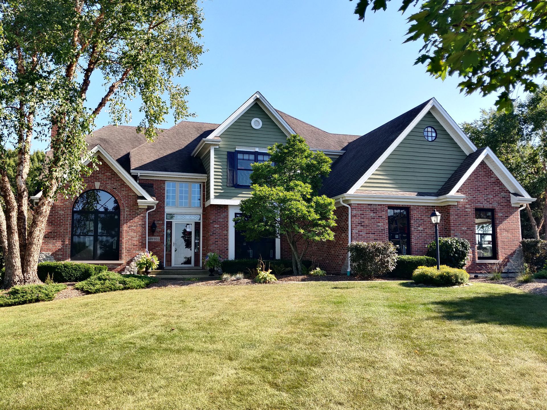 Two-story brick home with green siding, arched windows, and a grassy lawn on a sunny day.