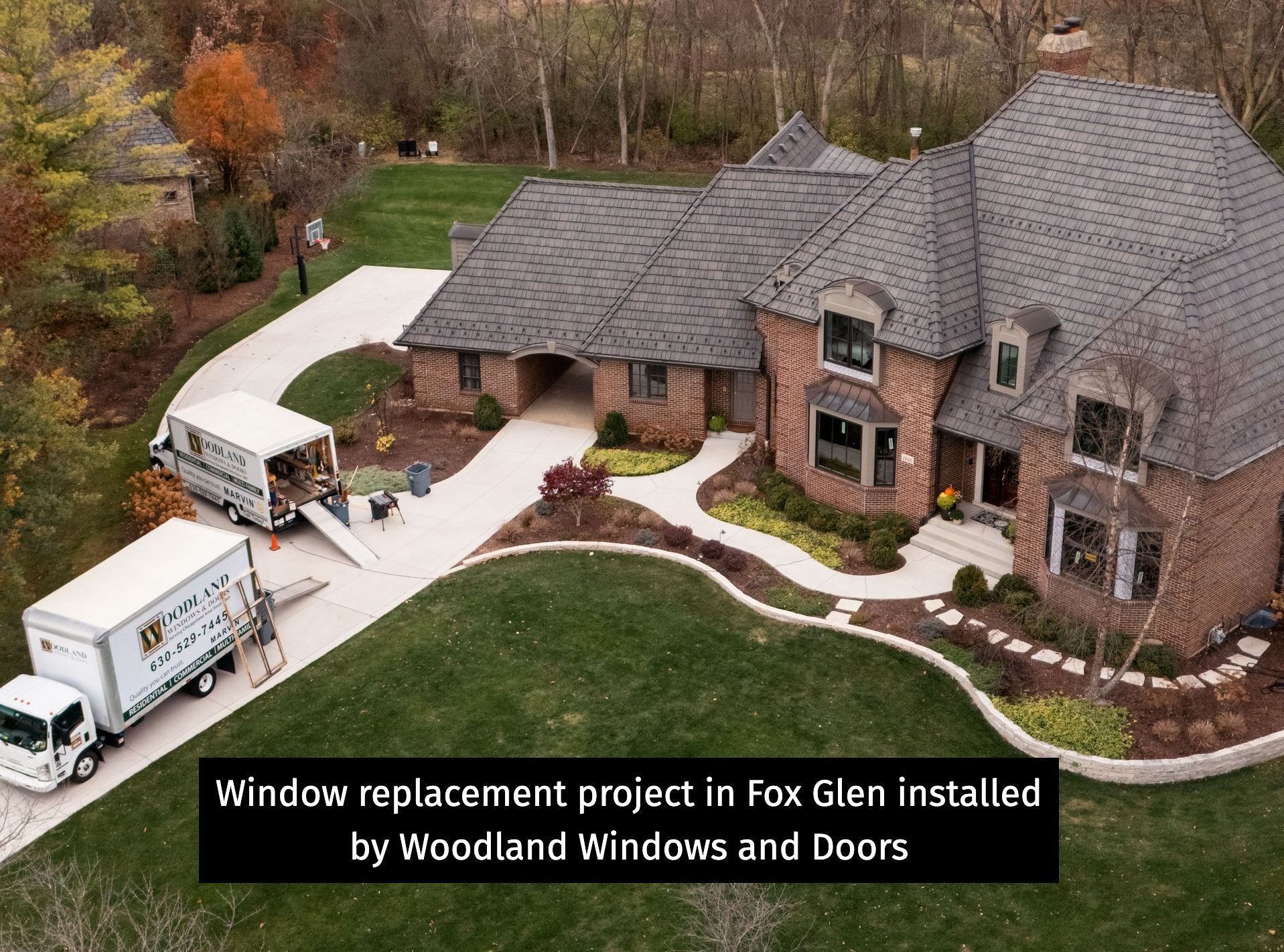 Window replacement at a brick house in Fox Glen by Woodland Windows and Doors; two trucks parked on the driveway.