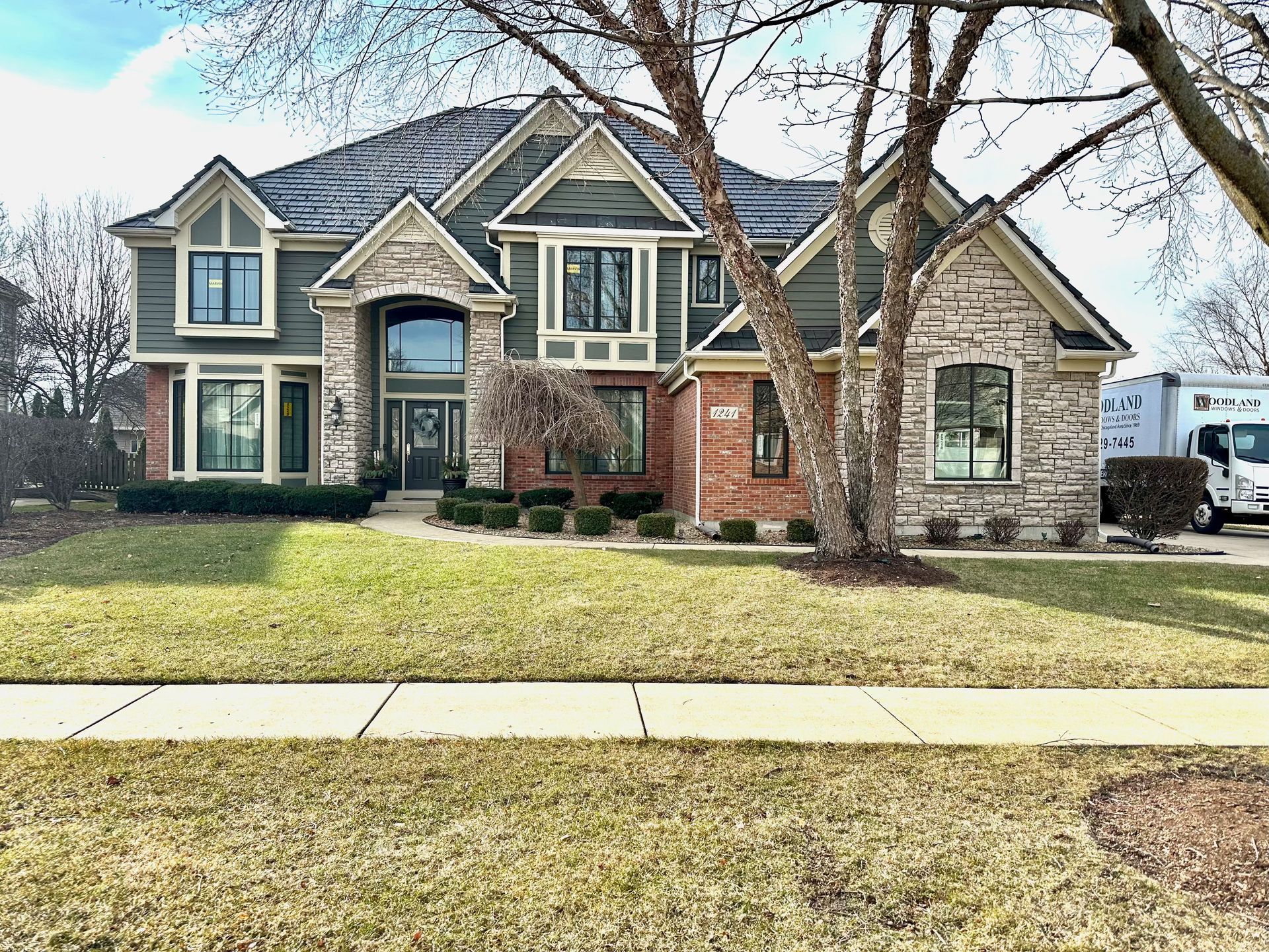 Large two-story house with green siding, stone facade, and a moving truck in the driveway.